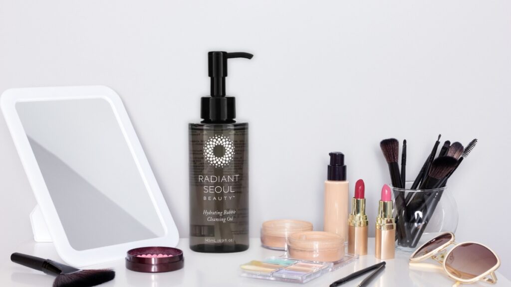 Radiant Seoul Hydrating Bubble Cleansing Oil bottle on a vanity table surrounded by makeup and brushes, a skincare essential for removing dirt and makeup.
