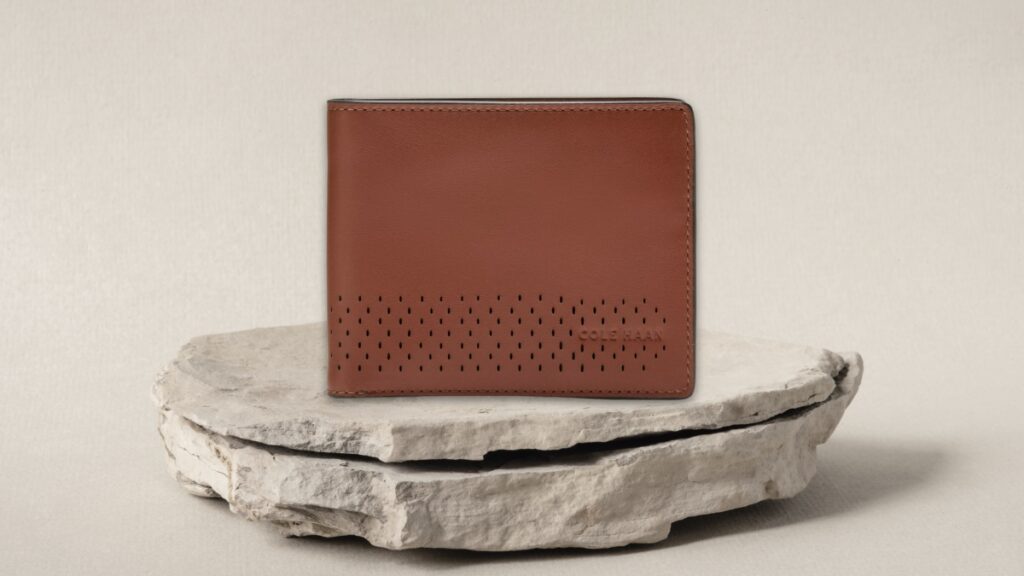 A brown Cole Haan leather wallet with a dotted design sits on a stone surface.