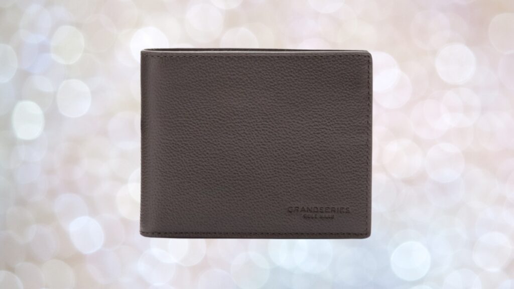 A gray Cole Haan GRANDSERIES leather wallet with a smooth, pebbled texture shown against a soft bokeh background.